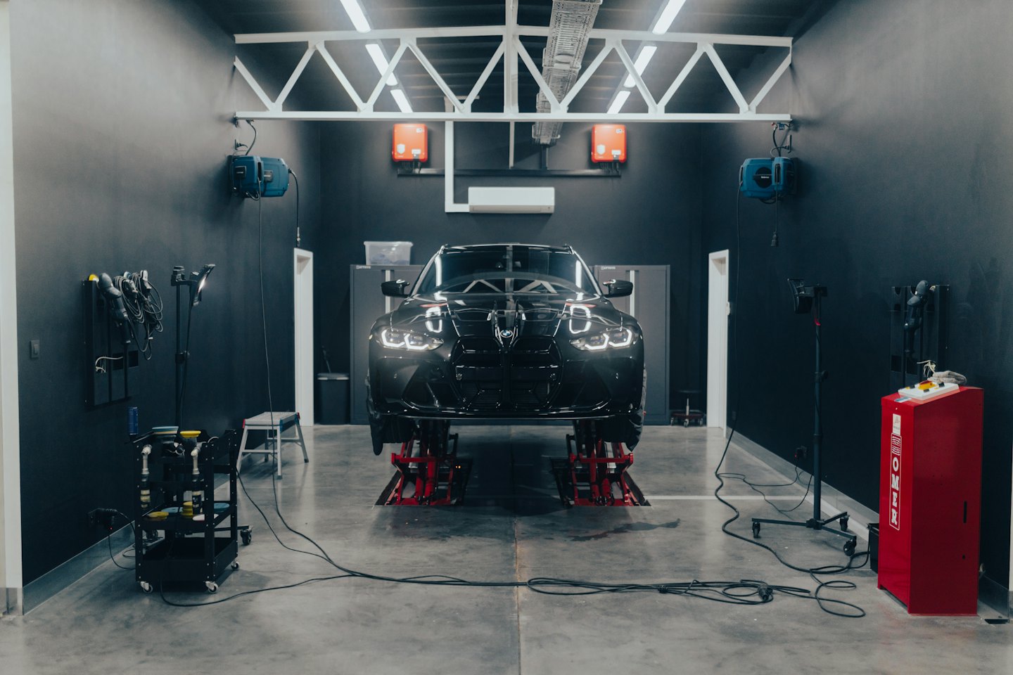 Zwarte luxe auto op hydraulische liften in een werkplaats.